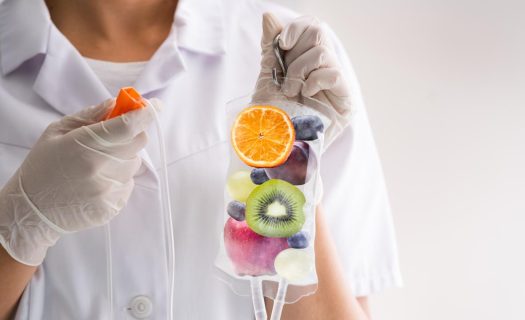 A healthcare professional holds an iv bag filled with various fruits like oranges, kiwis, and blueberries, symbolizing vitamin infusion.