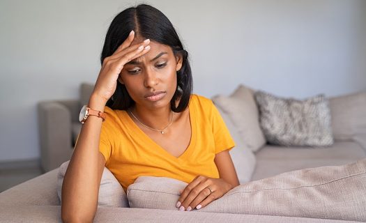 A woman sitting on a couch looking stressed with her hand on her forehead.