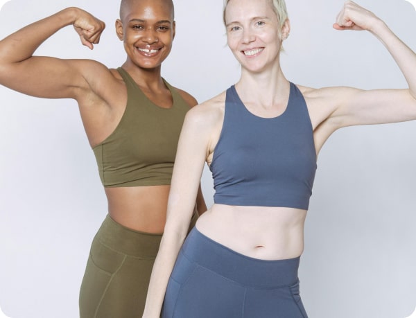 Two women in sportswear flexing their muscles and smiling against a plain background.