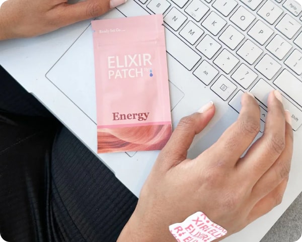 Person using a laptop with an "elixir patch energy" product and a patch applied on their hand visible.