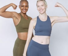Two women in sportswear flexing their muscles and smiling against a plain background.