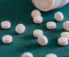 White pills scattered next to an open bottle on a teal fabric surface.