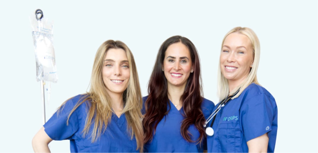 Three female healthcare professionals in blue scrubs, standing together with a white background, one holding a stethoscope.