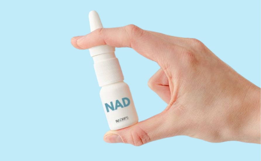 A hand holding a small white nasal spray bottle labeled "nad" against a light blue background.