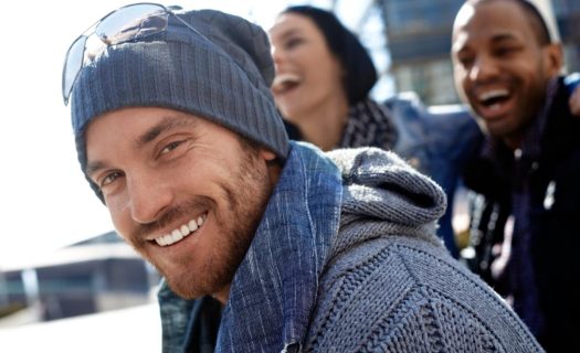 A smiling man in a beanie and scarf with friends laughing in the background.